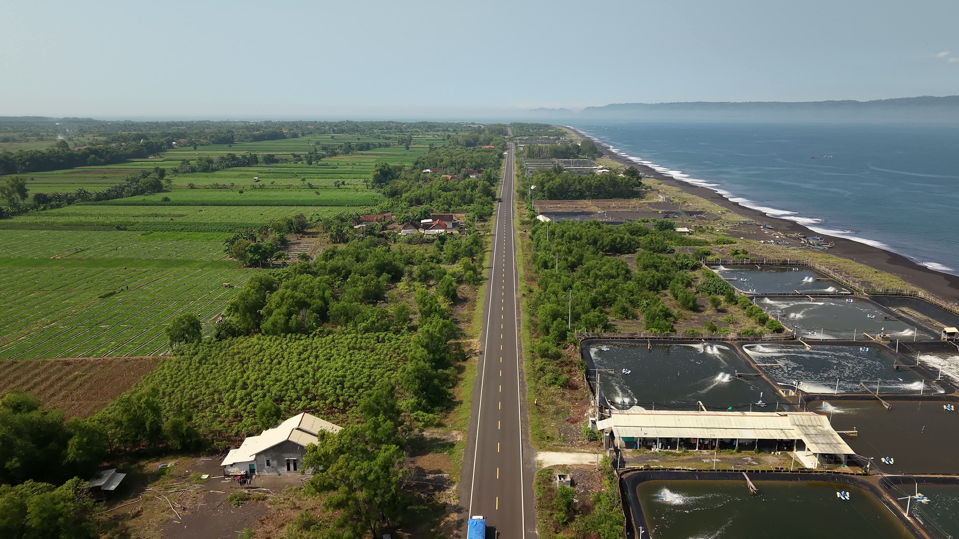 A straight coastal road beside the ocean and black-sand beach, Indonesia